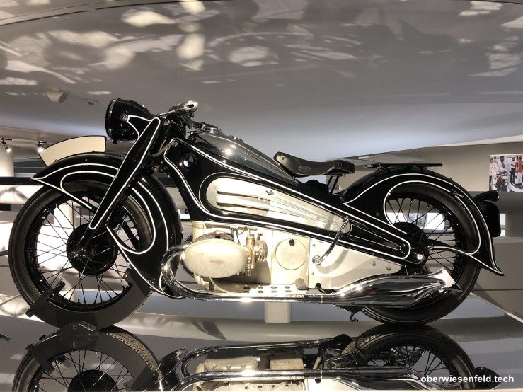 Ein elegantes Motorrad der Marke BMW mit einem kunstvollen Design und einer glänzenden schwarzen und silbernen Farbgebung, ausgestellt in einem modernen Raum.
